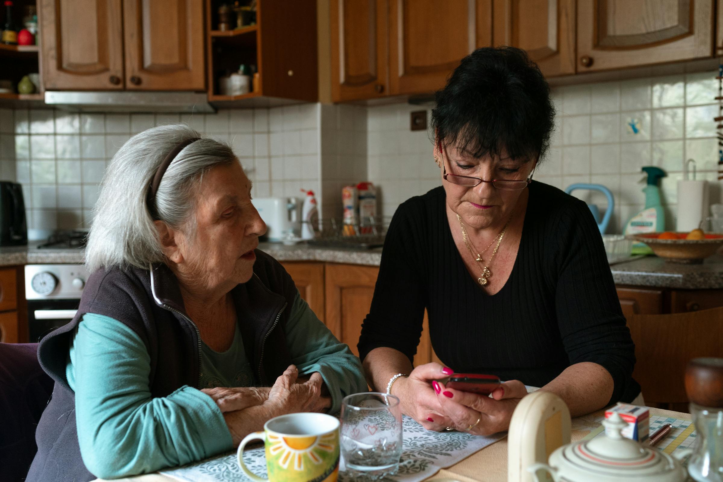 A senior woman and a caregiver share a quiet moment in a warm home kitchen.