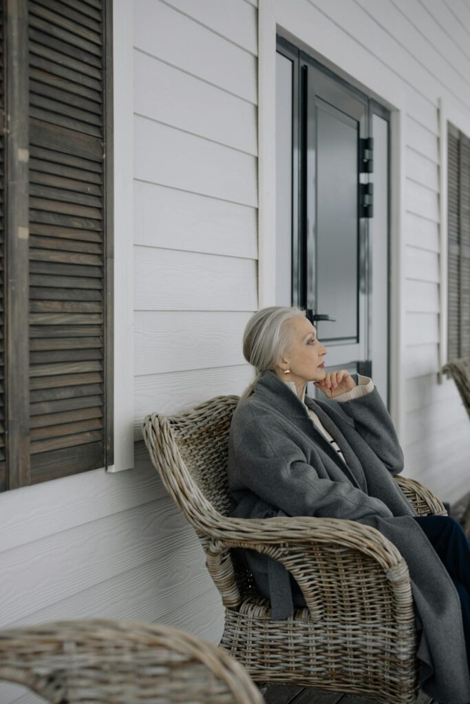 An elderly woman relaxing in a wicker chair on her porch.