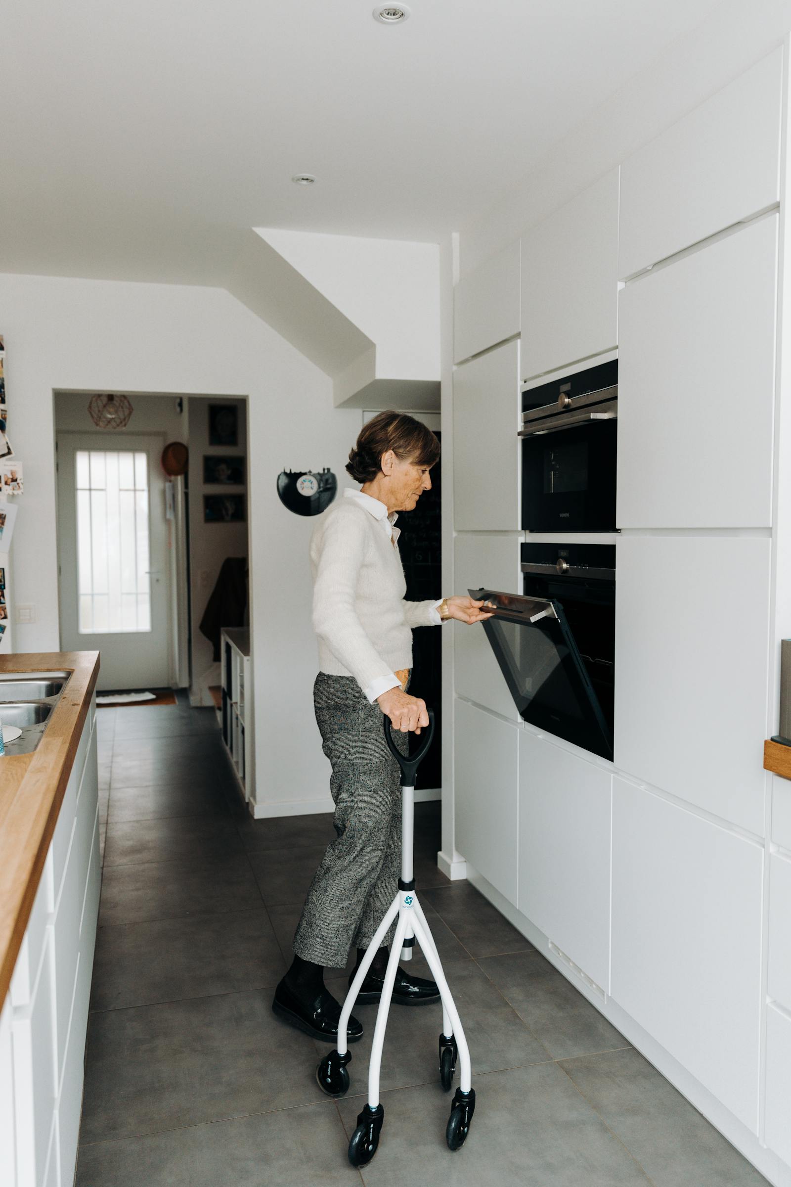 Senior woman using a walker while baking in a sunlit kitchen, recovering at home with independence.